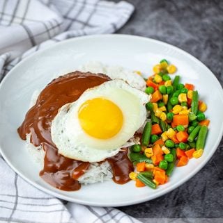 Hawaiian dish loco moco with vegetables on a white plate