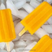 three homemade mango popsicles on the tray with ice