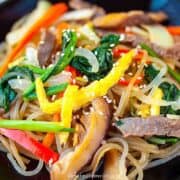 japchae Korean glass noodle on a black plate close up