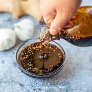 teriyaki sauce pouring from a glass bottle into a glass container with ginger and garlic background