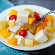 almond jello with mixed fruits on a sliver spoon in a bowl