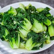 easy baby bok choy stir fry on a white plate with a stripe gray towel