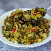 a scoop of stir fried pickled mustard greens on a sliver spoon