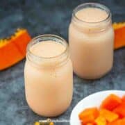 2 glass of papaya milk in jars with papaya at the background