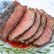 cooked medium rare prime rib roast slices up on chopping board with fresh rosemary